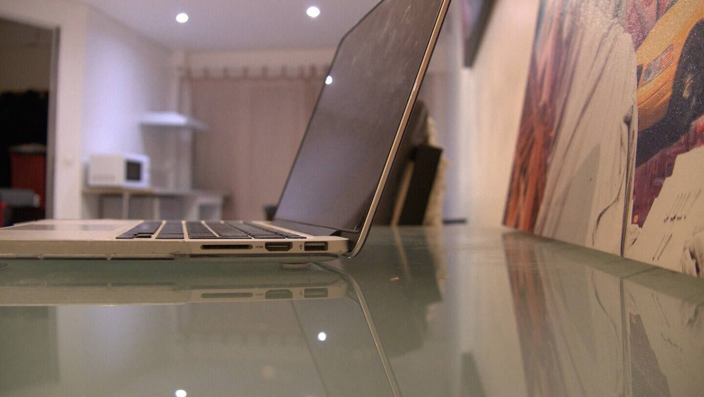 Un ordinateur portable posé sur une table en verre, avec un arrière-plan flou comprenant un four à micro-ondes et un tableau.