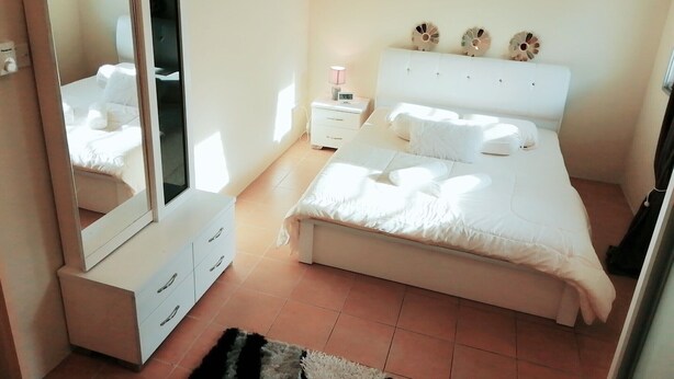 Ein Schlafzimmer mit einem Bett, einem Schminktisch, einem Nachttisch, einem Spiegel und Dekoration am Kopfteil.