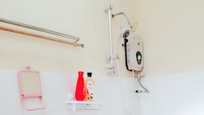 Ein Badezimmer mit einem weißen Waschbecken, einer Dusche und einer Toilette. Auf einem Regal liegen Pflegeprodukte und es gibt einen Handdesinfektionsspender.
