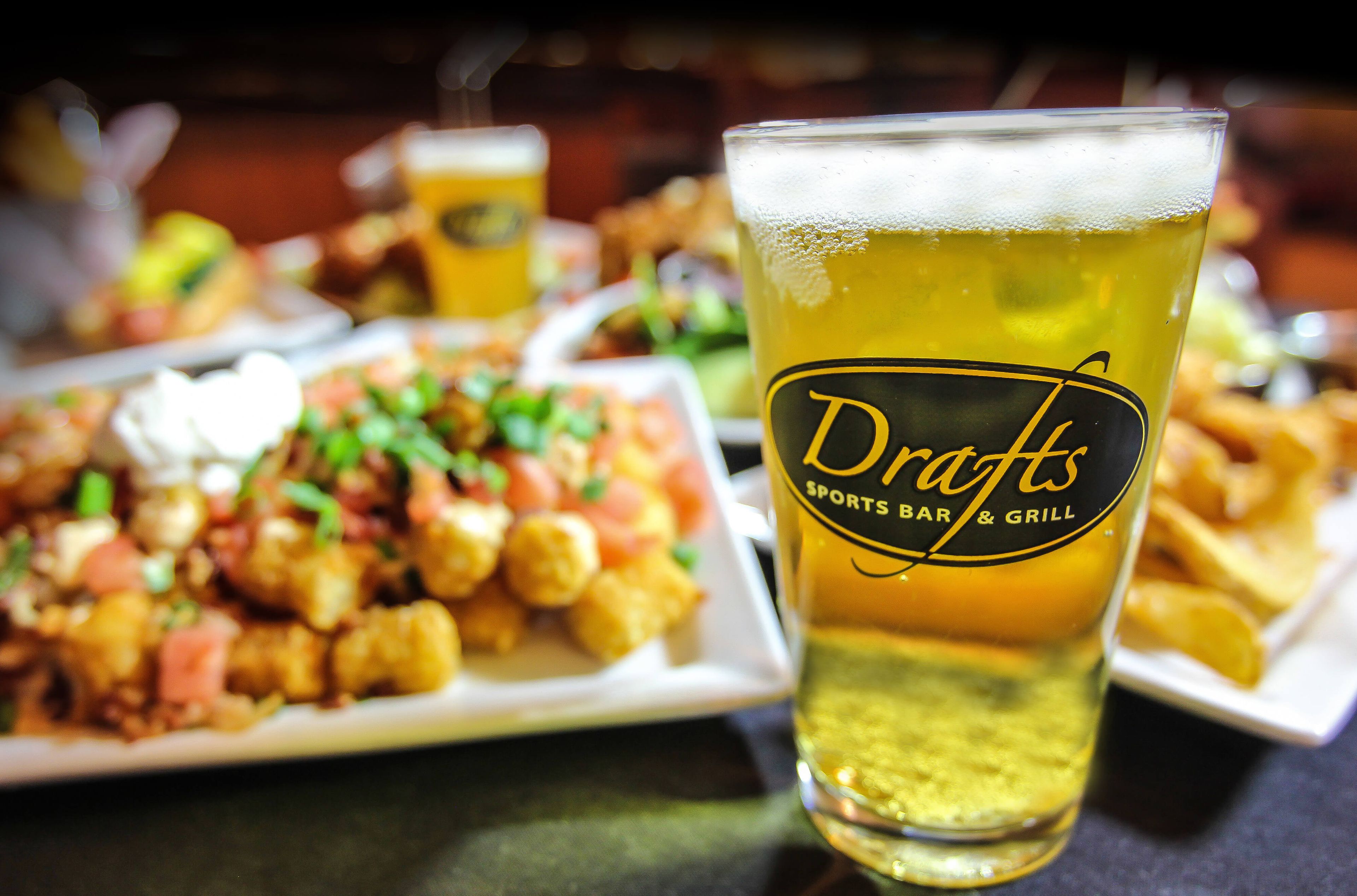A glass of beer with a label reading 'Drafts Sports Bar & Grill' and a plate of food in the background.