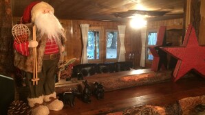 Interior rústico com teto de madeira, sofá de couro preto, estrela vermelha decorativa e um boneco de Papai Noel segurando uma bengala.