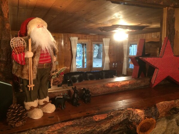 A rustic interior with a wooden ceiling, a black leather sofa, a red star decoration, and a Santa Claus figurine holding a cane. - Historic 1922 Cabin with Modern Amenities (Idyllwild-Pine Cove)