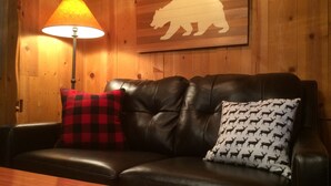 Um sofá de couro com duas almofadas estampadas, uma luminária e uma silhueta de urso na parede.