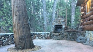 Lareira de pedra com parede de pedra e uma grande árvore numa área arborizada.