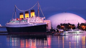 A large ship docked at a port with a hotel and a dome-shaped building in the background.
