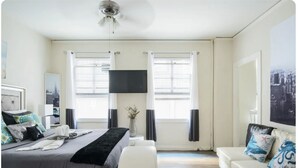 A hotel room with a bed, a sofa, a flat-screen TV, and a cityscape view.