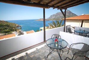 Una terraza con una mesa y sillas, con vistas a un paisaje costero y una montaña al fondo.