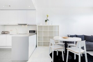 Een moderne keuken met witte kastjes, een magnetron en een eethoek met een ronde tafel en witte stoelen.