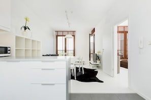 A modern kitchen with white cabinetry, a microwave, and a dining area with chairs.