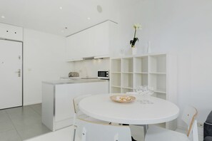Una cocina moderna con muebles blancos, un microondas y un comedor con una mesa redonda y sillas.