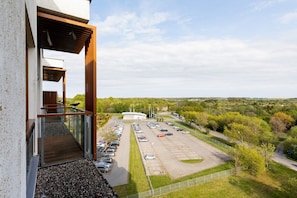 A building with a balcony overlooking a parking lot and a green landscape.