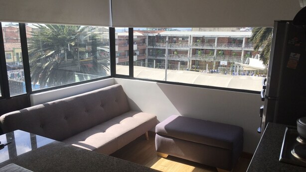 A modern kitchen with a large window, a beige sofa, and a small bench. - FLAT CHAPINERO CENTRAL (Bogotá)