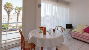 Una habitación con una mesa de comedor preparada para dos personas, un sofá, un televisor y un balcón con palmeras.