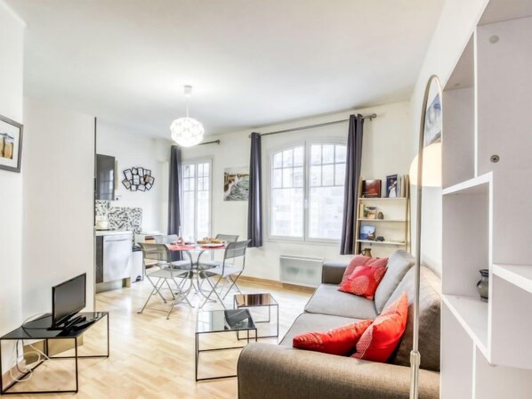 Un salon moderne comprenant un canapé, une table basse et une table à manger avec des chaises. Il y a également un coin cuisine avec un réfrigérateur et un four à micro-ondes.