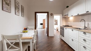 Eine moderne Küche mit weißen Schränken, ein Essbereich mit einem Marmortisch und ein Flur, der in einen anderen Raum führt.