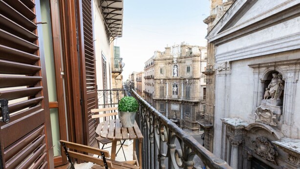 Ein Balkon mit einer Holzbank, einem Blumentopf und Blick auf historische Gebäude.