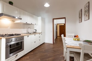 A modern kitchen with white cabinets, a stainless steel range, and a dining area with a marble table.