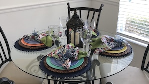 A glass-top dining table with a candle centerpiece, surrounded by chairs with cushioned seats.