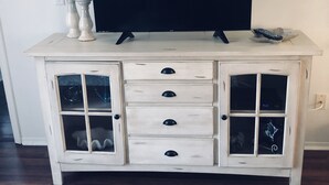 A white wooden cabinet with drawers and glass doors, a flat-screen TV on top, and a remote control on the right side.