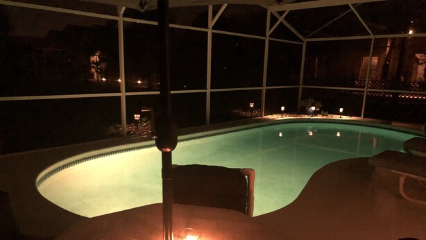 A pool area with a curved edge, a ceiling light fixture, and three candles on a table.