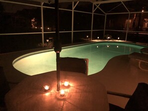 Ein Poolbereich mit geschwungener Kante, einer Deckenleuchte und drei Kerzen auf einem Tisch.