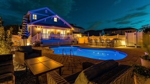 Una casa con piscina, mobiliario de exterior y un porche iluminado.