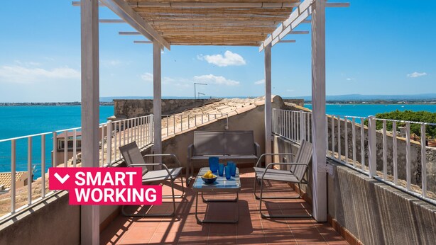 A balcony with a view of the sea, a table with chairs, and a sign reading "SMART WORKING". - Aretusa Apartment with Terrace by Wonderful Italy (Siracusa)
