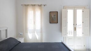 A bedroom with a bed, a nightstand, a lamp, a window with sheer curtains, a framed picture on the wall, and a door. - Aretusa Apartment with Terrace by Wonderful Italy (Siracusa)
