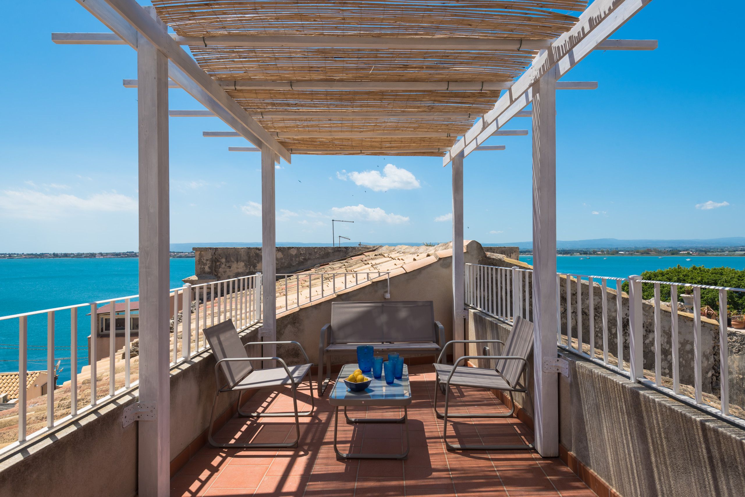 Een terras met uitzicht op zee, voorzien van stoelen en een tafel, en een pergola erboven.