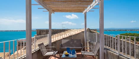 Una terrazza con vista sul mare, arredata con sedie e un tavolo, e un pergolato sovrastante.