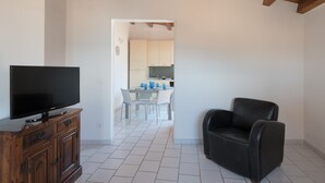 A living room with a flat-screen TV on a wooden cabinet, a black leather sofa, and a kitchen visible through an open doorway. - Aretusa Apartment with Terrace by Wonderful Italy (Siracusa)