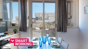A modern kitchen with a dining area, featuring a glass table set for six, a stove, and a view of the neighborhood through large windows. - Aretusa Apartment with Terrace by Wonderful Italy (Siracusa)