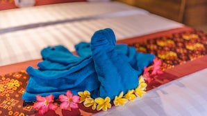 A bed with a neatly folded blue towel and a floral bedspread. - Nerima Hut Lembongan (Lembongan Island)