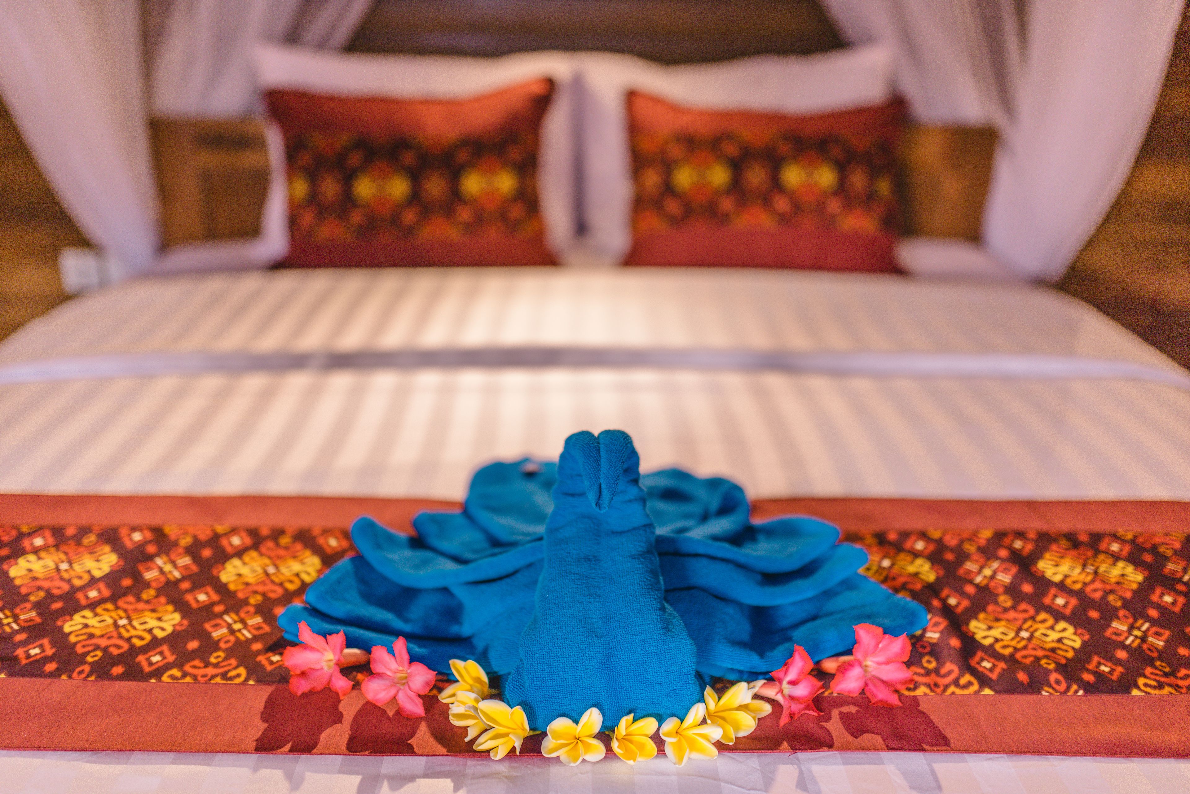 Ein ordentlich bezogenes Bett mit blauem Handtuch und dekorativen Blumen.