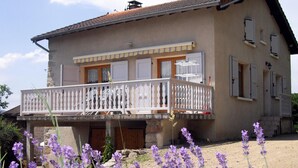 A two-story house with a balcony, a stone facade, and a small garden with purple flowers. - Traditional cottage with terrace, pets allowed (La Tuilière)