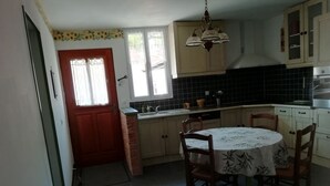A compact kitchen with a dining table and chairs, a red door, and a window with curtains. - Gite for 4 adults and a cot in the Isle valley (ST Martin l'Astier)