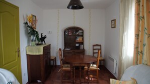 A dining area with a wooden table and chairs, a hanging light fixture, a bookshelf, and a yellow door. - Gite for 4 adults and a cot in the Isle valley (ST Martin l'Astier)
