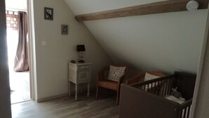 A room with a sloped ceiling, a wooden beam, a desk with a lamp, two chairs, and a crib. - Gite for 4 adults and a cot in the Isle valley (ST Martin l'Astier)