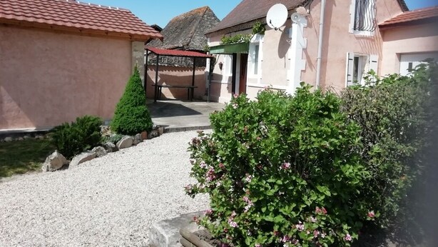 A residential building with a gravel driveway, a small garden with pink flowers, and a satellite dish on the roof. - Gite for 4 adults and a cot in the Isle valley (ST Martin l'Astier)