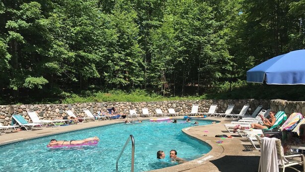 Une piscine entourée d’un mur de pierre et d’arbres, avec des chaises longues et des parasols.
