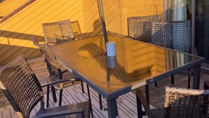 Une terrasse extérieure avec une table à plateau de verre, des chaises en osier et un grand parasol.
