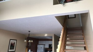 Un intérieur à plusieurs niveaux, avec un escalier, un coin cuisine et des plantes suspendues.