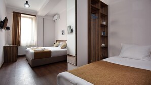 Habitación de hotel con dos camas, un armario de madera, un espejo, un radiador y una ventana con cortinas.