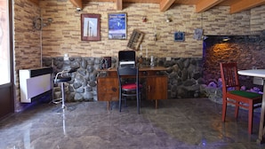 Una habitación con pared de piedra, techo de madera y un escritorio con dos sillas. Hay cuadros enmarcados en la pared y una chimenea de piedra.