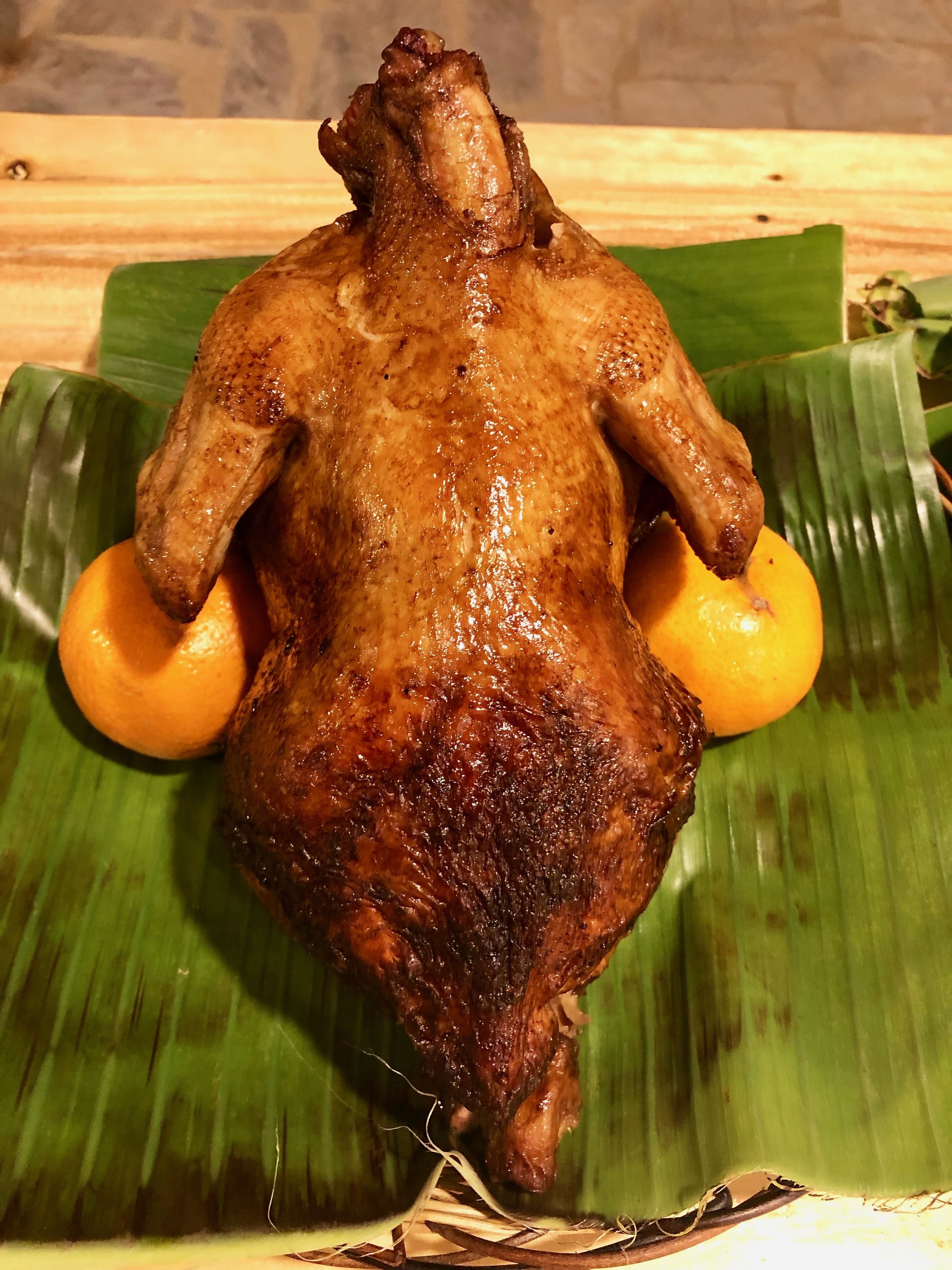 A roasted chicken on a banana leaf with two oranges.