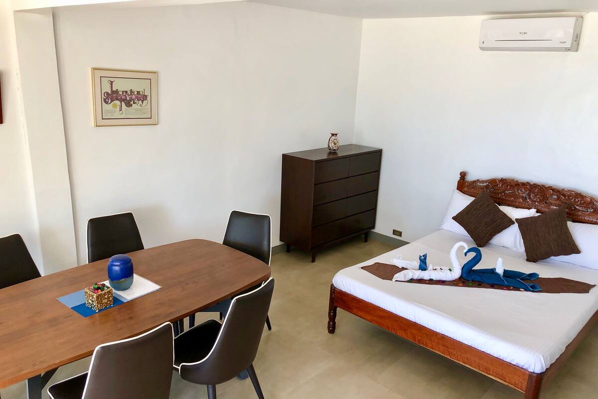 Een hotelkamer met een houten bed, een houten bureau en een dressoir. Er hangt een ingelijst certificaat aan de muur.