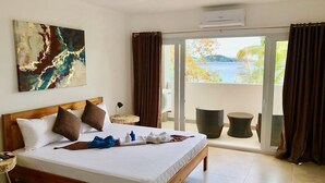 Een hotelkamer met een bed, een schilderij, een klein tafeltje met een lamp en uitzicht op de omgeving door een schuifdeur.