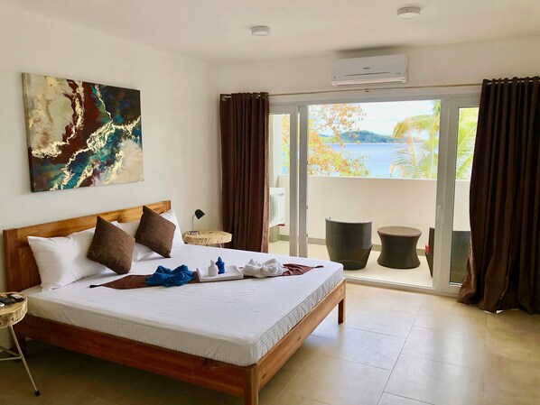 Una habitación de hotel con cama, un cuadro, una mesita con lámpara y vistas al exterior por una puerta corredera.