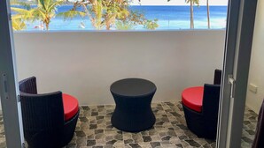 Een balkon met rieten stoelen en een tafel, met uitzicht op een strand met palmbomen en de oceaan.