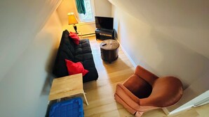 Een knus woongedeelte met een zwarte bank, een houten tafel, een blauwe opbergkist en een bruine fauteuil.